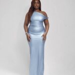 Woman wearing Aure, a fitted blue one-shoulder asymmetric knot dress by XELENE. Floor-length pencil silhouette.